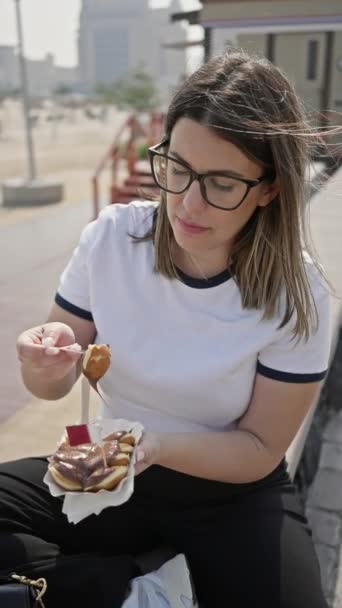 Eine junge brünette Frau genießt ein Schokoladendessert auf einer sonnigen Straße und verkörpert genussvolle Reiseerlebnisse. - Filmmaterial, Video