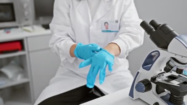 Μια στοχευμένη γυναίκα επιστήμονας φορώντας εργαστηριακή ποδιά και γάντια ετοιμάζεται να χρησιμοποιήσει ένα μικροσκόπιο σε ένα σύγχρονο εργαστηριακό περιβάλλον. - Πλάνα, βίντεο