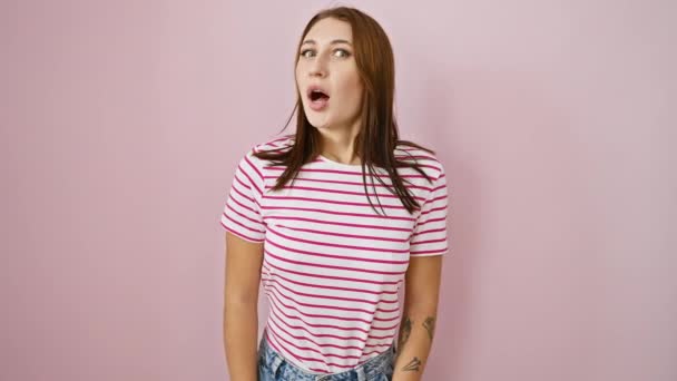 Çizgili tişörtlü, pembe arka planda yanak şişiren aptal esmer kız komik bir şekilde deli gibi surat yapıyor. eğlence ve güven dolu ifade - Video, Çekim