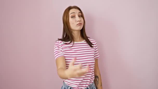 Naughty yet funny, young brunette girl in stripes tshirt, flaunting a rude 'fuck you' sign with middle finger, sheer provocation over isolated pink background, oozing attitude! - Кадри, відео