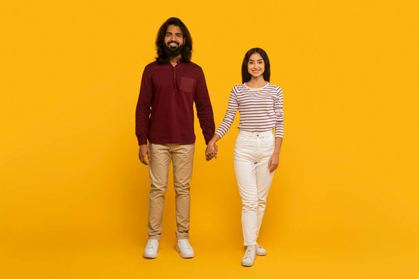 Un hombre y una mujer tomados de la mano y parados uno al lado del otro contra una pared amarilla, representando compañerismo - Foto, imagen