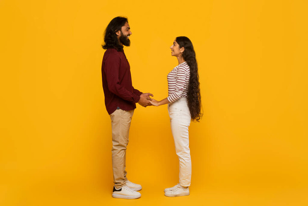 Ein Mann und eine Frau stehen sich Händchen haltend vor einem leuchtend gelben Hintergrund gegenüber und verkörpern ein Gefühl der Verbundenheit und Zusammengehörigkeit. - Foto, Bild