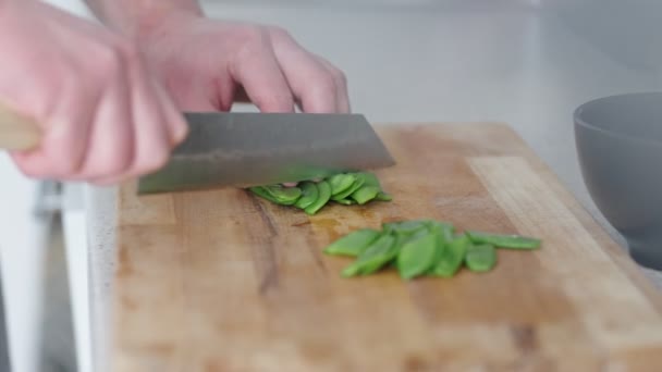 Close-up van de handen fijn hakken van verse groene erwten op een houten snijplank in een moderne keuken, met de nadruk op gezond koken en maaltijdbereiding. - Video