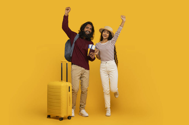 Pareja alegre con equipaje celebrando planes de viaje brazos levantados sobre un fondo amarillo vivo - Foto, Imagen