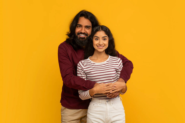 Uomo con le braccia intorno a una donna, entrambi sorridenti calorosamente su un solido sfondo giallo - Foto, immagini