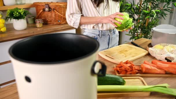 Egy fiatal nő zöldségeket újrahasznosít egy komposzt kukában. Háziasszony ételt főz és szerves hulladékot komposztál egy bokasi konténerben otthon. Ökológiai és fenntarthatósági koncepció - Felvétel, videó