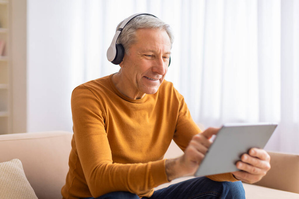 Starší muž se soustředí na tablet s nasazenými sluchátky, což naznačuje, že si možná užívá multimédia nebo se učí něco nového - Fotografie, Obrázek