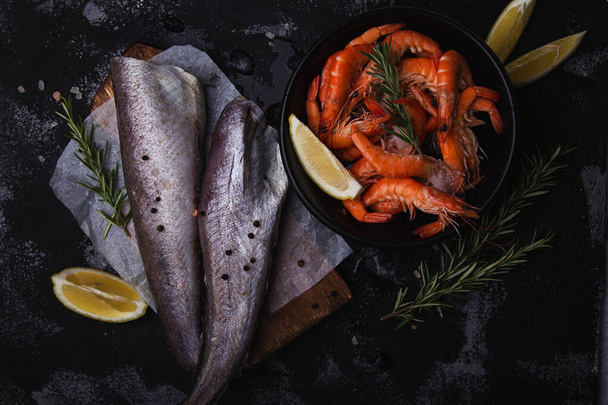 Arreglo de mariscos frescos con gambas y merluza de pescado sobre fondo oscuro, ideal para presentaciones culinarias. - Foto, imagen