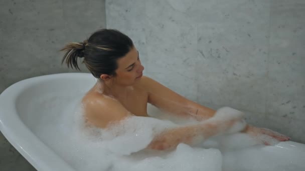 Een serene vrouw geniet van een ontspannend bad in een schone, marmeren badkamer, die rust en zelfzorg uitstraalt. - Video