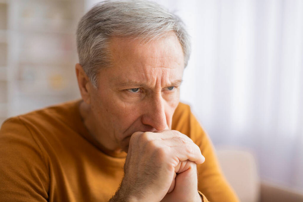 Een oudere man houdt zijn nek vast, een teken van spanning of pijn, mogelijk door een slechte houding of een onderliggend gezondheidsprobleem. - Foto, afbeelding