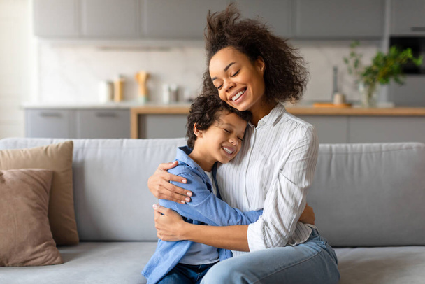 Usmívající se žena a její syn se objímají v jasně osvětleném obývacím pokoji - Fotografie, Obrázek