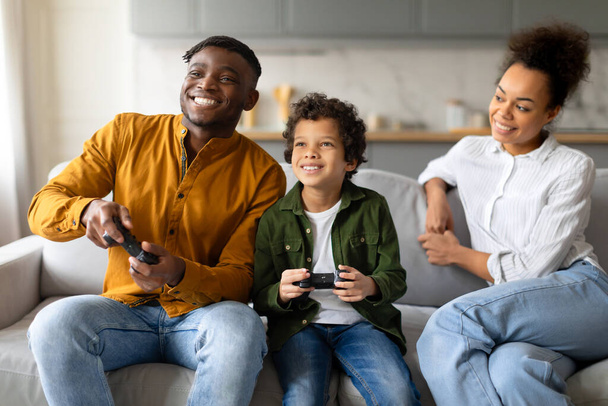 Eine Familie versinkt in einer lustigen Spielsitzung zusammen auf dem Sofa, mit Spielcontrollern in der Hand - Foto, Bild