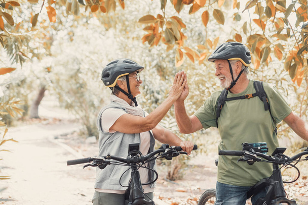 Kilku z dwóch seniorów daje pięć razem na świeżym powietrzu zabawy z rowerów korzystających z natury. Para starszych ludzi buduje zdrowy i sprawny tryb życia. - Zdjęcie, obraz