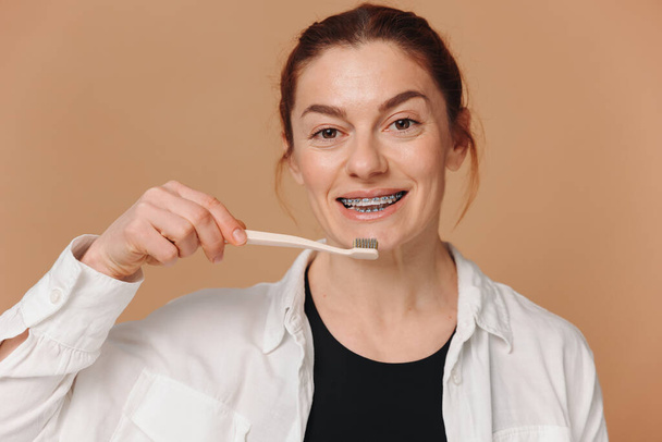 Onnellinen kypsä nainen hammasraudat tilalla hammasharja beige tausta - Valokuva, kuva