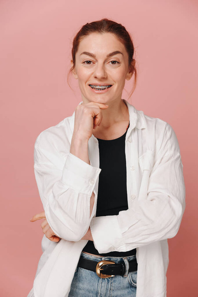 Modern boldog nő bemutató mosoly fogszabályzóval rózsaszín háttér - Fotó, kép