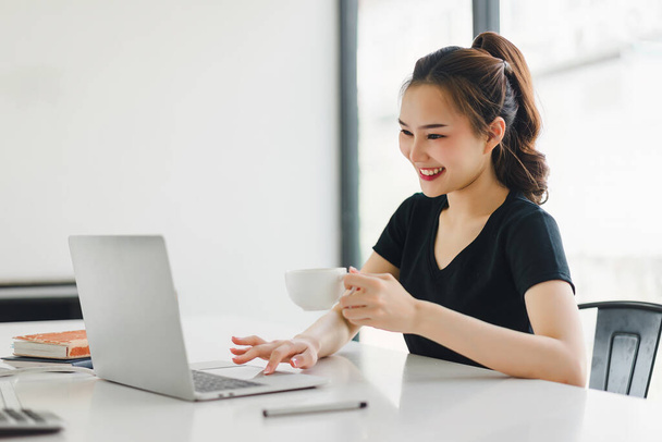 Mulher de negócios asiática bem sucedida parece confiante e sorri enquanto trabalha com laptop no escritório - Foto, Imagem