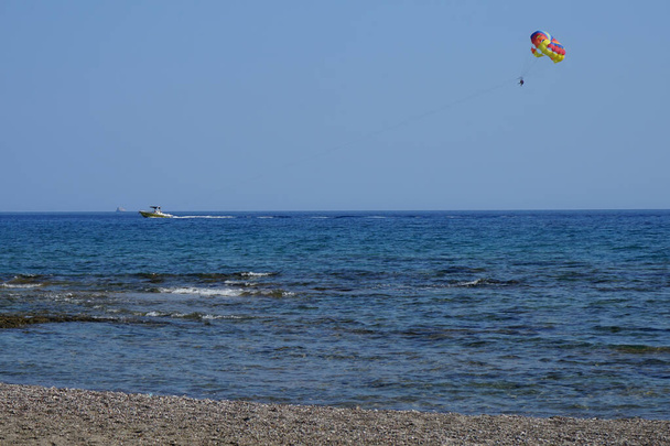 Paralotniarstwo na Morzu Śródziemnym. Parasailing, parascending, paraskiing lub parakiting, jest rekreacyjna działalność kiting, gdzie osoba jest holowana za pojazdem podczas przymocowania do specjalnie zaprojektowanego skrzydła baldachimowego. Rodos, Grecja  - Zdjęcie, obraz