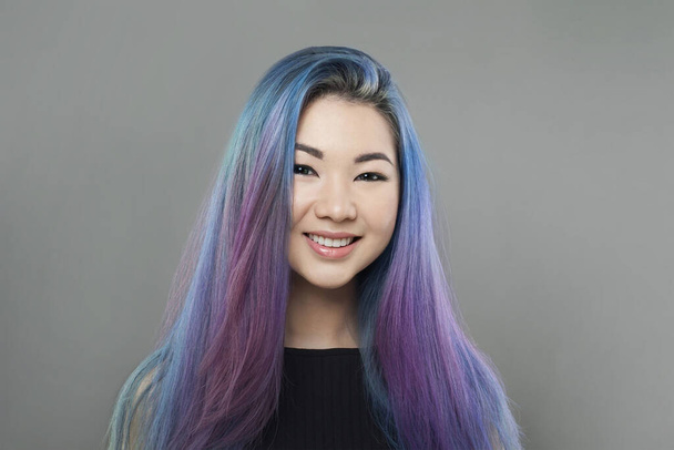 Junge glückliche asiatische Frau mit bunt gefärbten blauen und lila Haaren auf grauem Hintergrund, Porträt - Foto, Bild