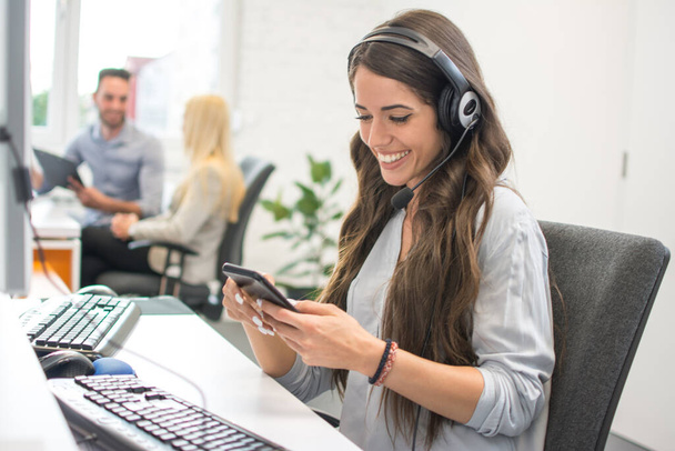Smiling young woman with headset using mobile phone in office - Photo, Image