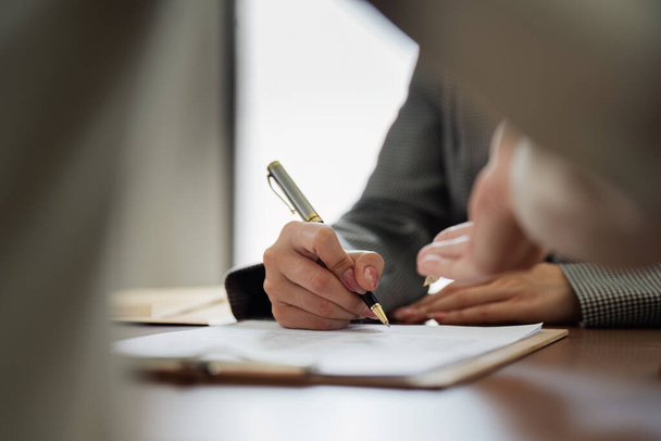 Ένας άνθρωπος γράφει με ένα στυλό σε ένα κομμάτι χαρτί. Ο άνθρωπος φοράει κοστούμι και γραβάτα. Έννοια της τυπικότητας και του επαγγελματισμού - Φωτογραφία, εικόνα