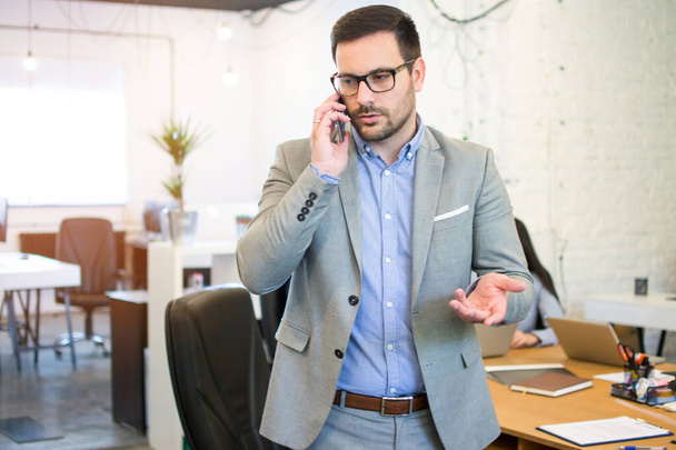 Красивий бізнесмен говорить на мобільному телефоні в офісі
 - Фото, зображення