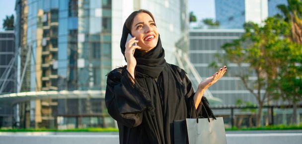 Красива арабська жінка з сумкою, що розмовляє на мобільному телефоні на вулиці - Фото, зображення