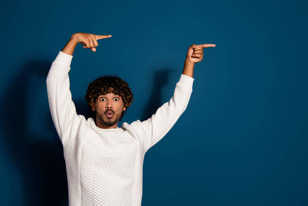 Photo of impressed shocked guy dressed white pullover pointing two fingers empty space isolated dark blue color background. - Φωτογραφία, εικόνα