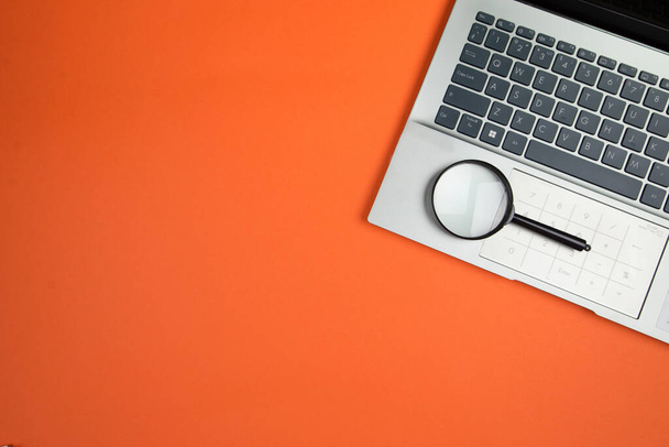 Teil einer Laptop-Tastatur mit Lupe auf orangefarbenem Hintergrund, Draufsicht, Kopierraum, Platz für Text. - Foto, Bild