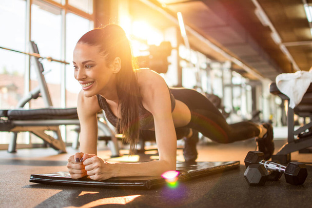 bela slim fit jovem mulher em roupas esportivas fazendo prancha exercício no tapete no ginásio. - Foto, Imagem