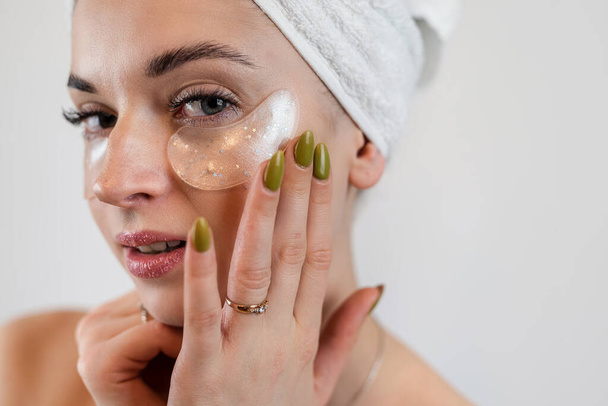Donna caucasica toccare la pelle luminosa viso con macchie di idrogel sotto gli occhi isolati su bianco. Macchie oculari antirughe - Foto, immagini