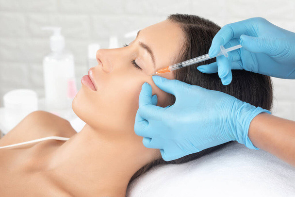 Cosmetologist makes rejuvenating anti wrinkle injections on the face of a beautiful woman. Female aesthetic cosmetology in a beauty salon. - Photo, Image