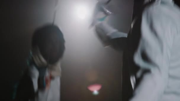 Задний ход неузнаваемого фехтовальщика, дерущегося с рапирой с фехтовальщицей в маске эпинефрина во время соревнований в тёмной туманной комнате - Кадры, видео