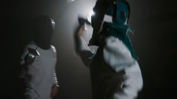 Медленно возвращаясь к женщине-фехтовальщице, нападающей на оппонента рапирой во время матча по фехтованию в темном туманном зале - Кадры, видео