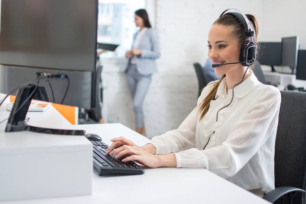 Friendly customer support operator with headset and microphone assisting to client in call centre - Photo, Image