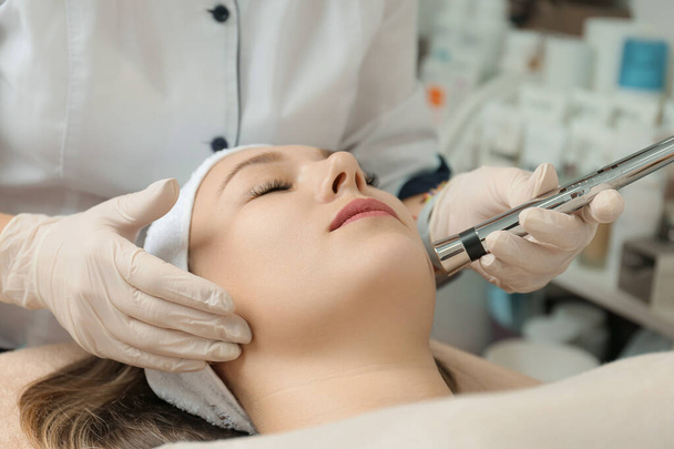 Rejuvenating facial therapy treatment at spa salon clinic. Young beautiful woman getting lifting anti-aging, face massage and skincare by electroporation facial therapy aesthetic cosmetology. - Fotó, kép