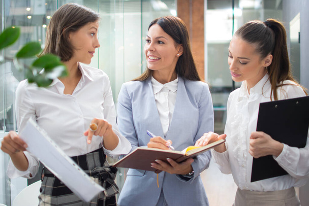 Drei schöne junge Geschäftsfrau diskutiert Dokumente, während sie durch Büro-Lobby geht - Foto, Bild