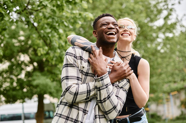 Una coppia multiculturale felice, un uomo afroamericano che tiene tra le braccia una donna caucasica all'aperto in un parco. - Foto, immagini