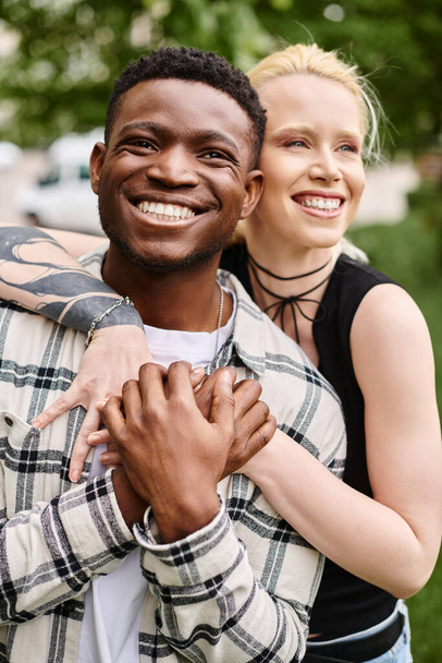 Ένα ευτυχισμένο πολυπολιτισμικό ζευγάρι - ένας Αφροαμερικάνος που κρατάει μια λευκή γυναίκα στην αγκαλιά του - σε μια ρομαντική αγκαλιά έξω σε ένα πάρκο. - Φωτογραφία, εικόνα