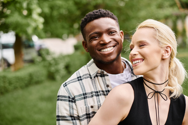 Ein fröhliches multikulturelles Paar, das in einem sonnenbeschienenen Park fröhlich lächelt. - Foto, Bild
