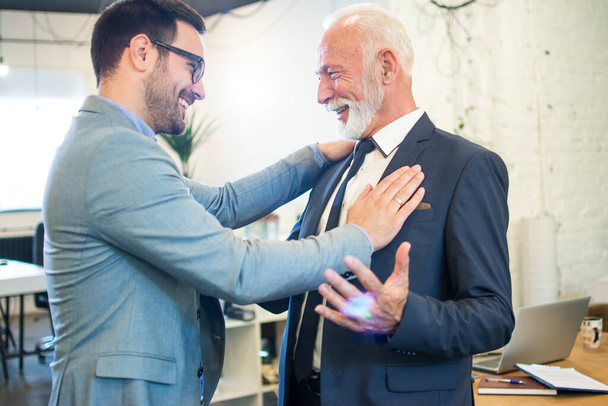 Счастливые бизнесмены приветствуют друг друга в офисе. Сотрудник среднего возраста, поздравляет своего наставника. - Фото, изображение