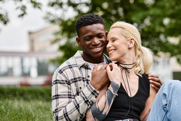 Multikulturelles Paar, ein afroamerikanischer Mann und eine kaukasische Frau, sitzen glücklich zusammen im Gras eines Parks. - Foto, Bild