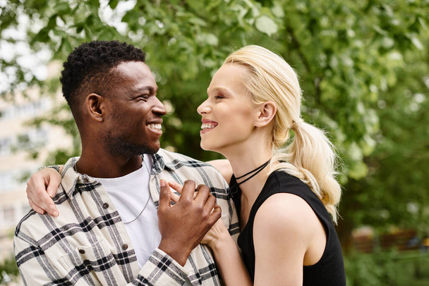 Egy vidám pillanat, melyet multikulturális párként örökítenek meg, őszinte mosolyt csal egy parkban.. - Fotó, kép