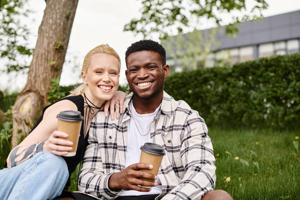 Πολυπολιτισμικό ζευγάρι, ένας Αφροαμερικάνος και μια λευκή γυναίκα, απολαμβάνοντας καφέ μαζί, ενώ κάθονται στο γρασίδι. - Φωτογραφία, εικόνα