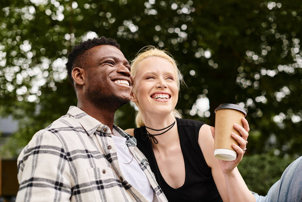A happy multicultural couple, an African American man and a Caucasian woman, sitting together outdoors in a park. - Photo, Image