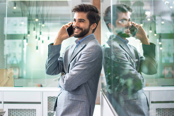 Młody, przystojny biznesmen rozmawiający przez telefon komórkowy w nowoczesnym biurze - Zdjęcie, obraz