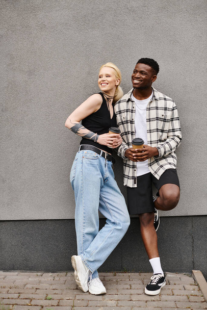 Een gelukkig stel, een multicultureel vriendje en vriendin, naast elkaar in een stedelijke straat bij een grijs gebouw. - Foto, afbeelding