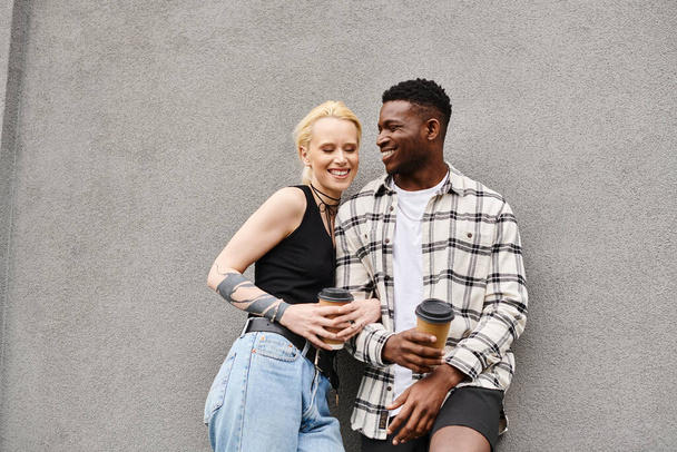 Um casal feliz e multicultural, um homem e uma mulher, estão juntos em uma rua urbana perto de um prédio cinza. - Foto, Imagem