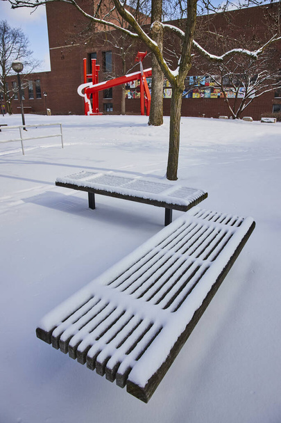 Ειρηνική σκηνή χειμώνα στο Fort Wayne, Ιντιάνα με φρέσκο χιόνι κουβέρτα στο παγκάκι πάρκο, άγονο δέντρο και ζωντανή δημόσια τέχνη - Φωτογραφία, εικόνα