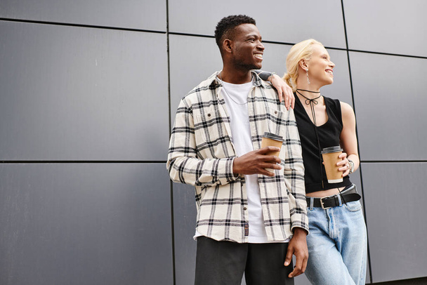 Egy boldog multikulturális pár, egy férfi és egy nő, akik egy városi utcában állnak egy szürke épület mellett.. - Fotó, kép