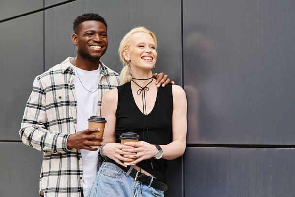 Un couple multiculturel, un homme et une femme, heureux ensemble dans une rue urbaine près d'un bâtiment gris. - Photo, image